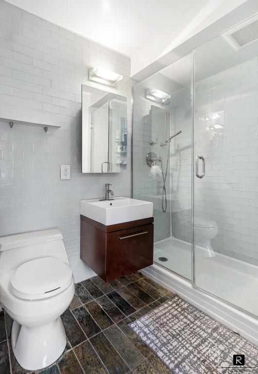 bathroom with tile walls, vanity, a shower with shower door, and toilet