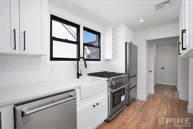 kitchen featuring visible vents, a sink, stainless steel appliances, white cabinetry, and light wood-type flooring