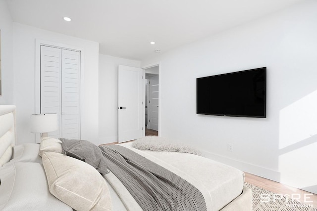 bedroom with a closet, recessed lighting, light wood-style flooring, and baseboards