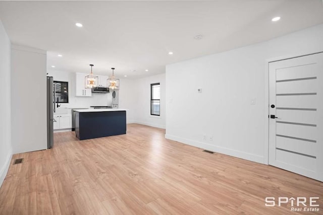 kitchen with pendant lighting, appliances with stainless steel finishes, a center island, light hardwood / wood-style floors, and white cabinets