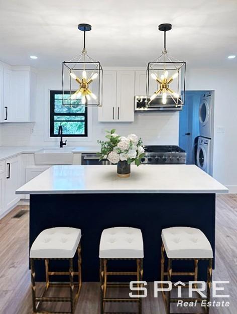 kitchen featuring stacked washer / dryer, a sink, a kitchen island, white cabinetry, and range