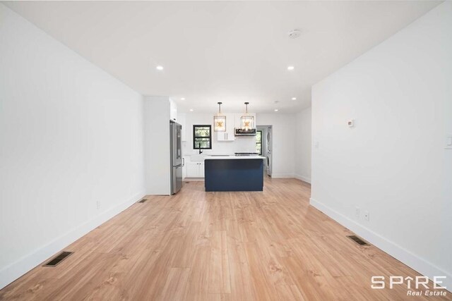 kitchen featuring visible vents, a center island, light wood-type flooring, freestanding refrigerator, and white cabinets