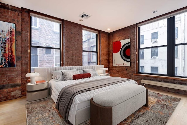 bedroom featuring light wood-type flooring, a wall of windows, and brick wall