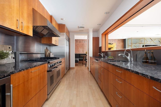 kitchen featuring range hood, light hardwood / wood-style flooring, dark stone counters, beverage cooler, and range with two ovens