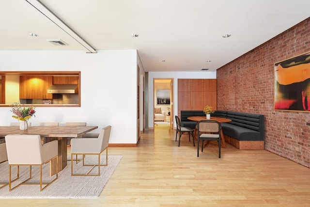 dining area with light hardwood / wood-style floors and brick wall