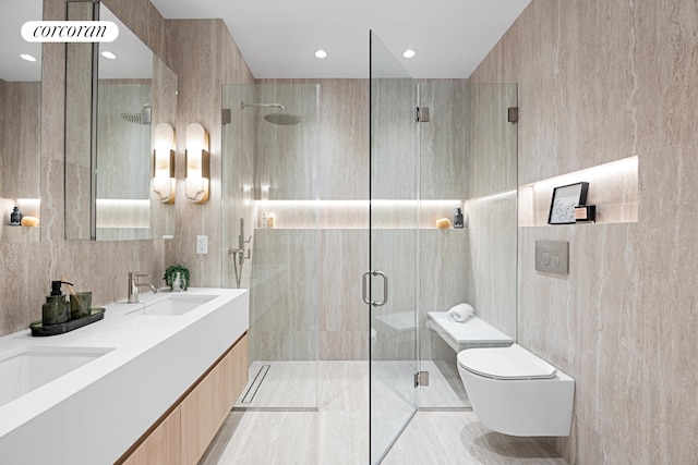 bathroom featuring toilet, a sink, tile walls, a shower stall, and double vanity