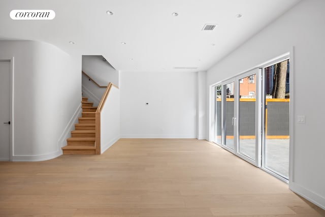 empty room with light wood-style flooring, stairs, and visible vents