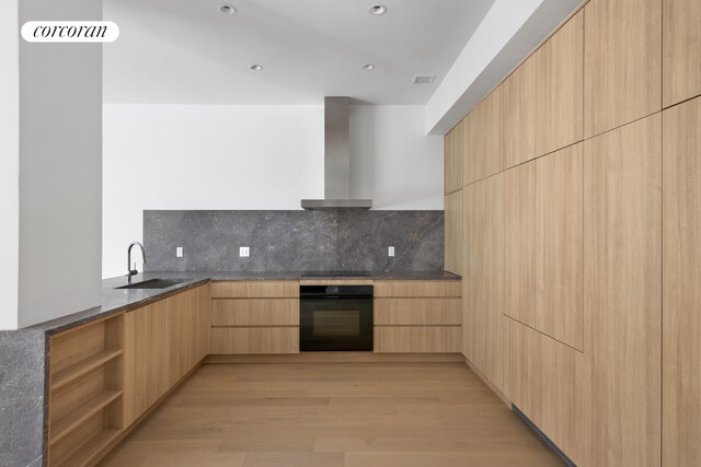 kitchen with a sink, wall chimney range hood, dark stone countertops, modern cabinets, and black appliances