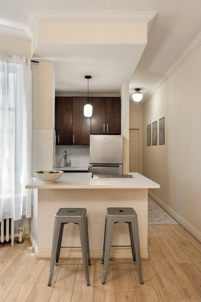 20 E 88th St Unit 2B, New York City, NY 10128 - kitchen with freestanding refrigerator, a kitchen breakfast bar, dark brown cabinetry, light countertops, and ornamental molding