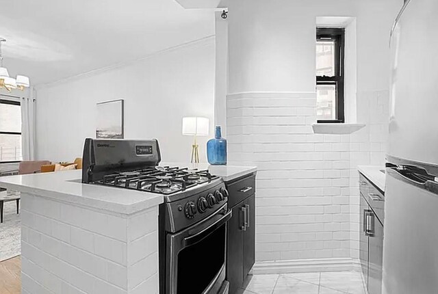 kitchen featuring tile walls, hanging light fixtures, stainless steel refrigerator, range with gas stovetop, and a notable chandelier