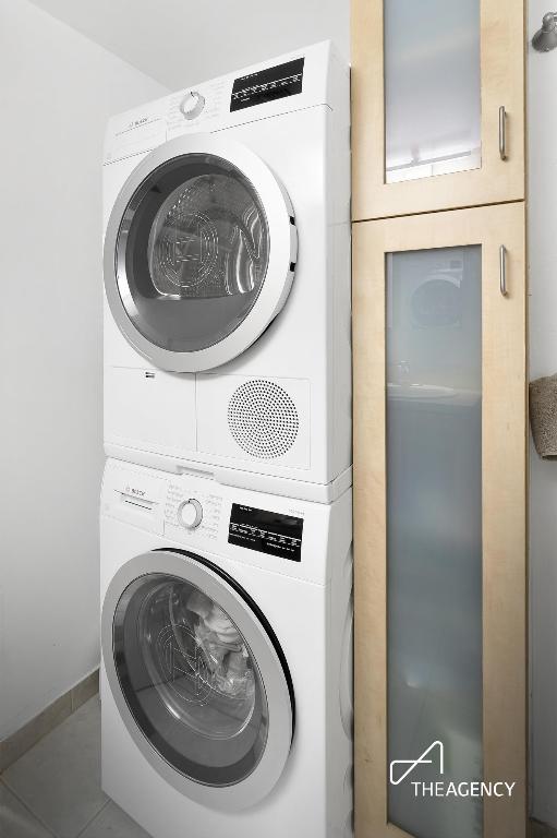 clothes washing area featuring tile patterned flooring and stacked washer and clothes dryer