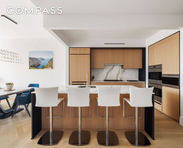 kitchen featuring a breakfast bar, decorative backsplash, double oven, gas cooktop, and modern cabinets