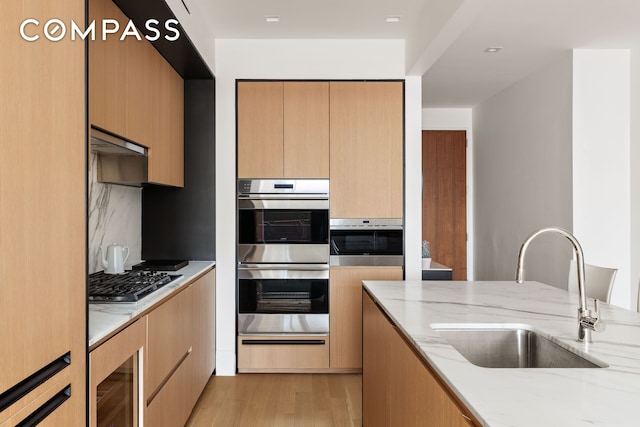 kitchen featuring light wood-style flooring, stainless steel appliances, a sink, light stone countertops, and a warming drawer