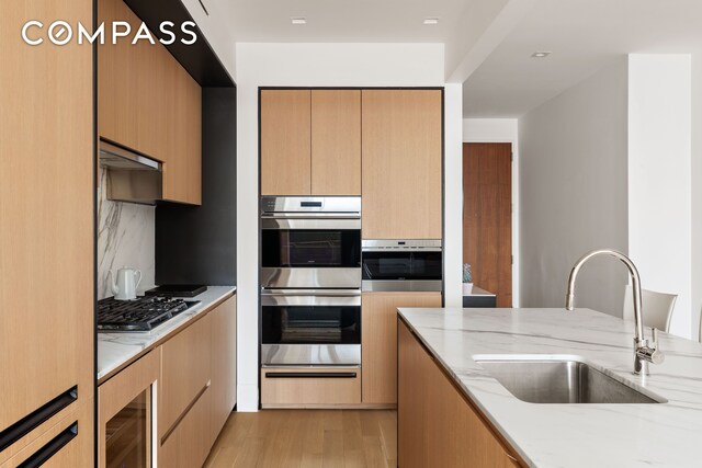 kitchen featuring wine cooler, appliances with stainless steel finishes, light stone countertops, a sink, and a warming drawer