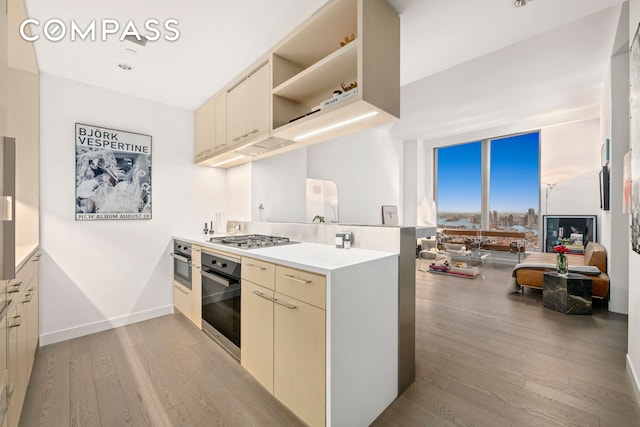 kitchen featuring cream cabinets, light wood-style flooring, stainless steel appliances, a peninsula, and light countertops