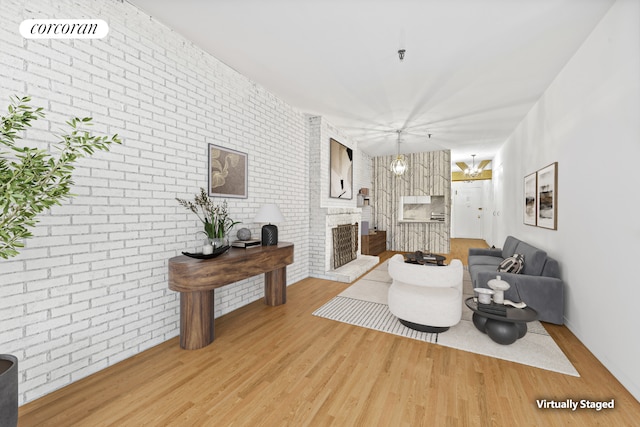 living area with a chandelier, a brick fireplace, light wood-style flooring, and brick wall