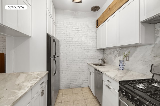 kitchen with light tile patterned floors, stainless steel appliances, brick wall, a sink, and white cabinets