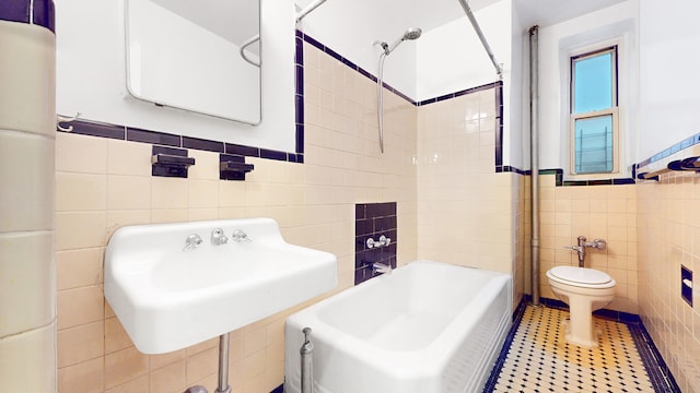 bathroom with tile patterned flooring, toilet, wainscoting, bathtub / shower combination, and tile walls