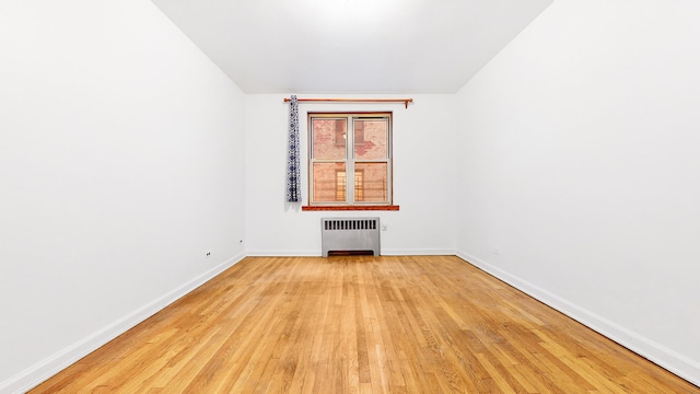 unfurnished room with light wood-type flooring, baseboards, and radiator heating unit