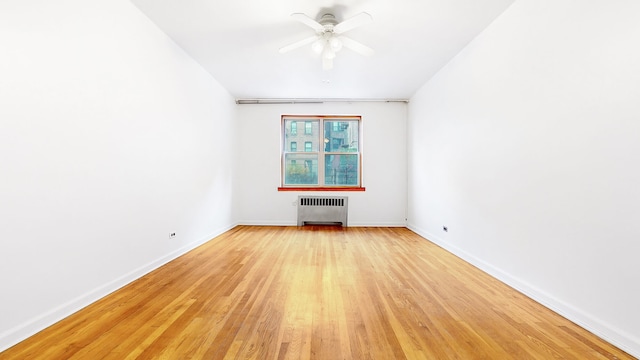 empty room with baseboards, light wood-style floors, ceiling fan, and radiator heating unit