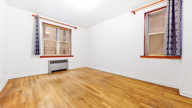 empty room with baseboards, radiator, and hardwood / wood-style flooring