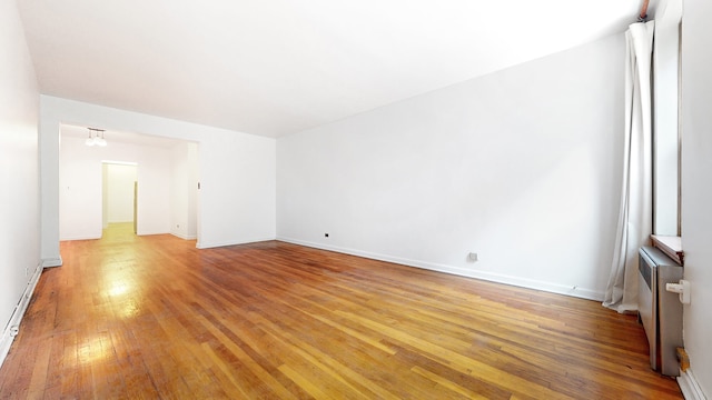 unfurnished room with light wood finished floors, a chandelier, radiator heating unit, and baseboards