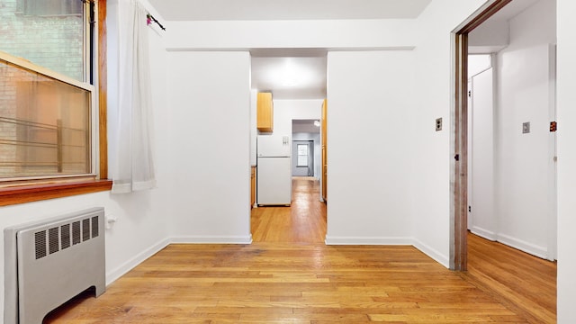 corridor with radiator, baseboards, and light wood-type flooring