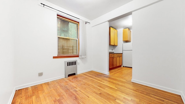 empty room featuring light wood-type flooring, baseboards, and radiator heating unit