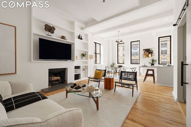 living room featuring an inviting chandelier, a barn door, light hardwood / wood-style flooring, and built in shelves