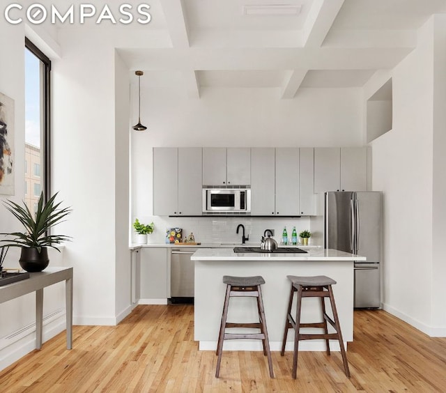 kitchen featuring appliances with stainless steel finishes, tasteful backsplash, a kitchen breakfast bar, gray cabinets, and a kitchen island with sink