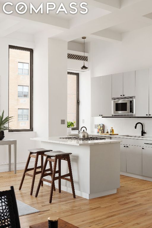 kitchen with a kitchen bar, light hardwood / wood-style floors, hanging light fixtures, and stainless steel appliances