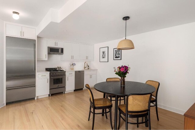 kitchen with decorative light fixtures, backsplash, high end appliances, white cabinetry, and light wood-type flooring