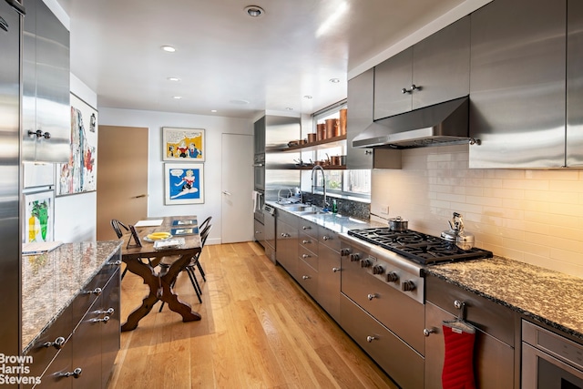 kitchen featuring stainless steel gas cooktop, light wood-style flooring, a sink, under cabinet range hood, and backsplash