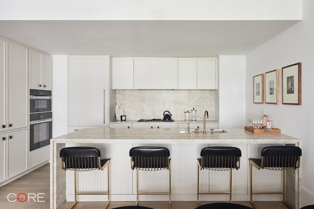 kitchen with white cabinetry, sink, light stone countertops, and a kitchen bar