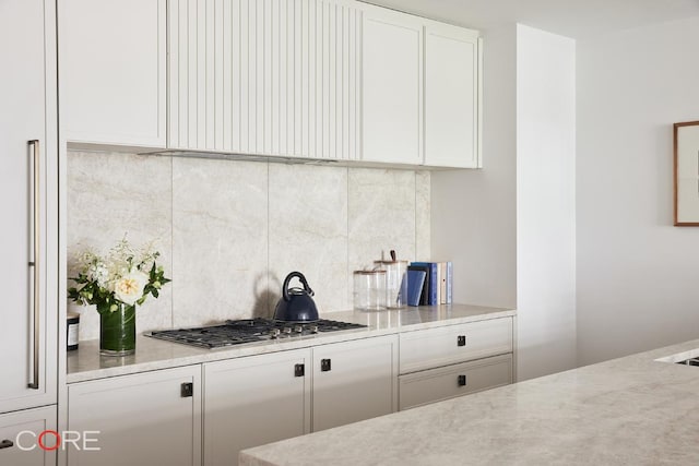 kitchen featuring stainless steel gas stovetop, light stone countertops, white cabinets, and backsplash