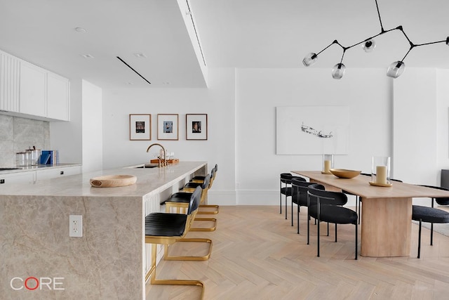 kitchen with sink, a breakfast bar, light parquet floors, white cabinetry, and an island with sink