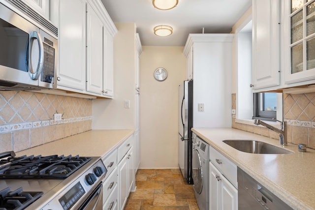 kitchen with washer / dryer, a sink, stainless steel appliances, stone finish floor, and white cabinets