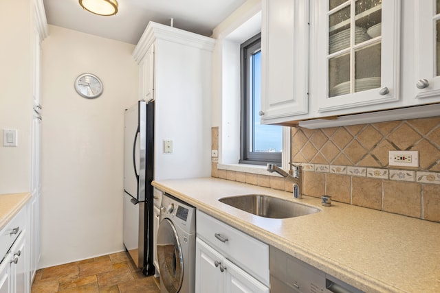 kitchen featuring washer / clothes dryer, a sink, light countertops, stone finish flooring, and white cabinetry