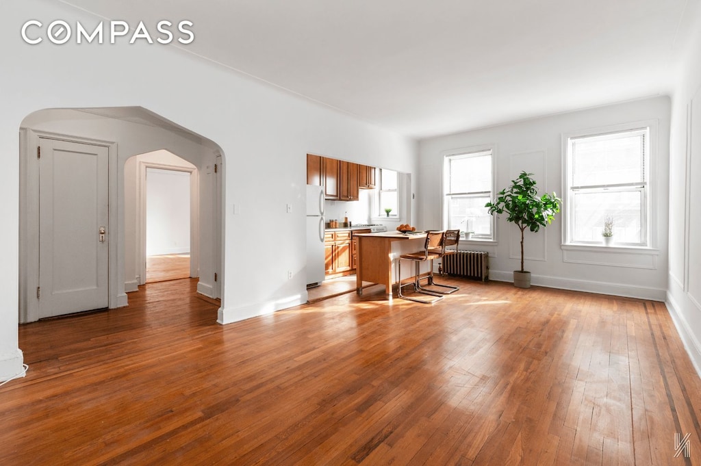 interior space featuring arched walkways, hardwood / wood-style floors, radiator heating unit, and baseboards