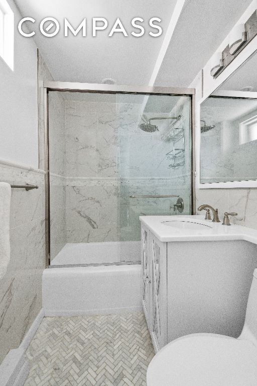 full bathroom featuring tile walls, vanity, toilet, and combined bath / shower with glass door