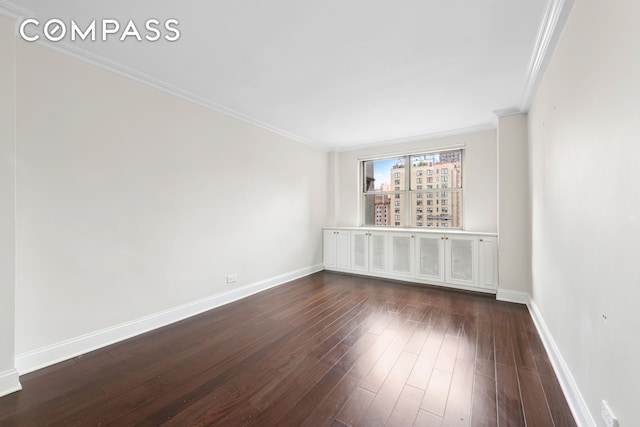 spare room with dark wood-style floors, ornamental molding, and baseboards