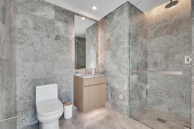 bathroom featuring a tile shower, vanity, tile walls, and toilet