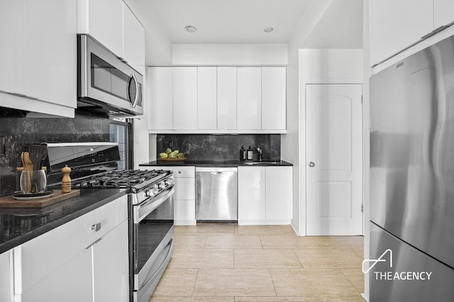 kitchen with dark countertops, white cabinetry, appliances with stainless steel finishes, and backsplash