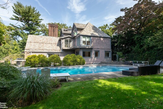 back of property featuring an outdoor pool, a lawn, a balcony, a chimney, and a high end roof