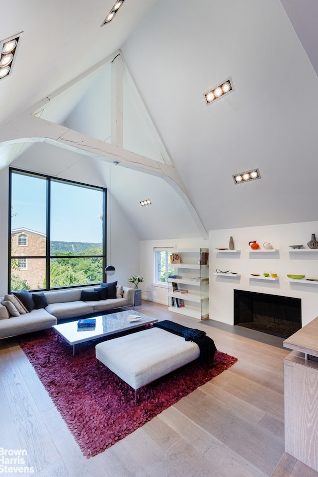 living room with high vaulted ceiling, light wood finished floors, beamed ceiling, and a fireplace