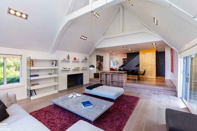 living area with high vaulted ceiling, built in shelves, wood finished floors, a fireplace with flush hearth, and beam ceiling