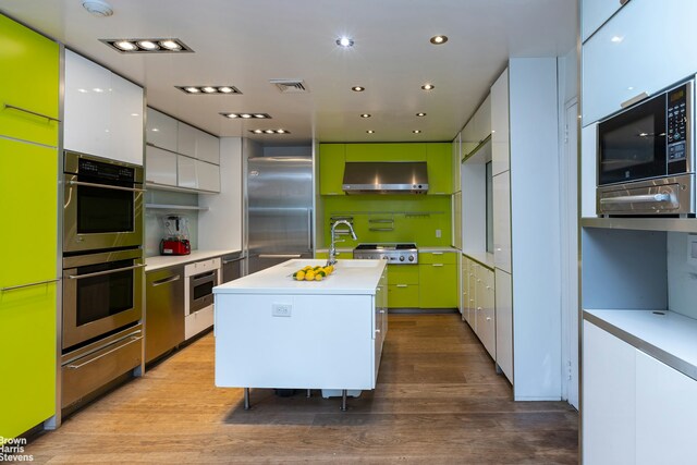 kitchen with range hood, light countertops, white cabinetry, an island with sink, and built in appliances