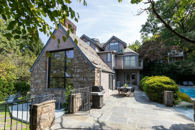 back of house with a chimney, outdoor dining area, a balcony, a patio area, and stone siding