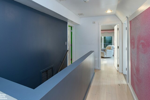 corridor featuring lofted ceiling, light wood-style flooring, an upstairs landing, and visible vents