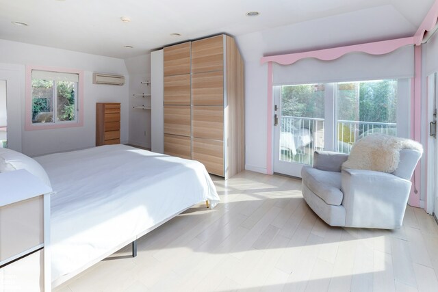 bedroom with a wall unit AC, access to exterior, multiple windows, and light wood-style floors